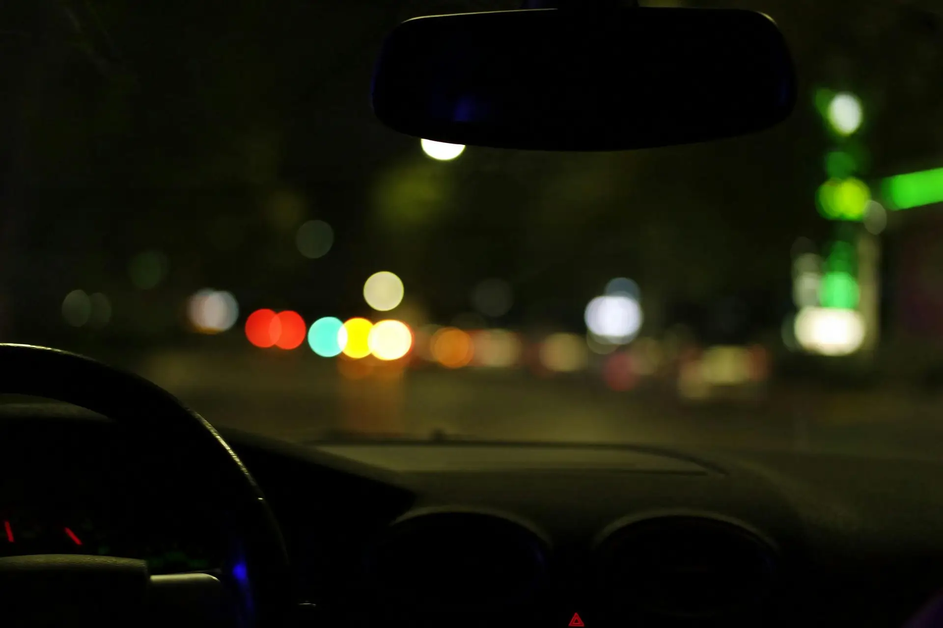 Blurred city lights seen from a car interior at night, depicting urban driving ambiance.