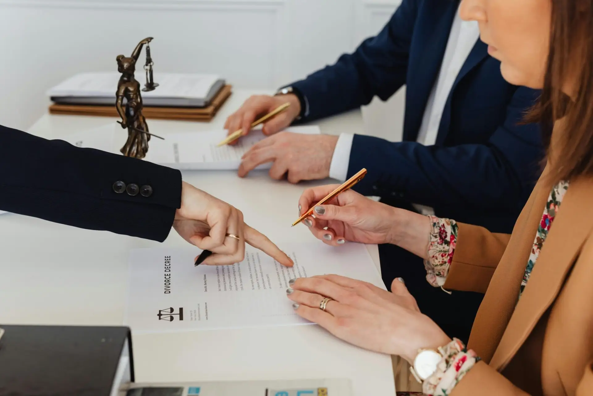 Hands signing a divorce decree, with a justice statue nearby, symbolizing legal proceedings.